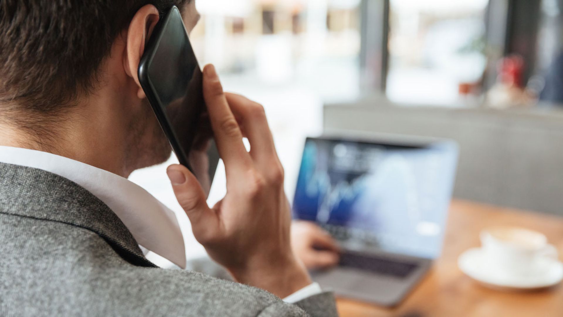 business man talking on smartphone while looking at laptop